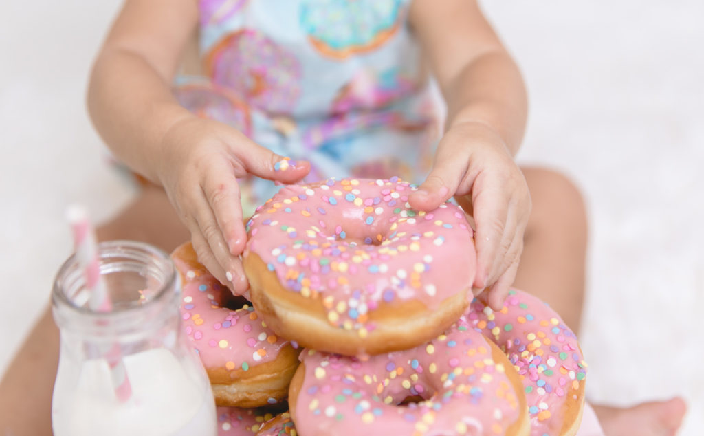 little girl reaching for a stack of pink sprinkle donuts