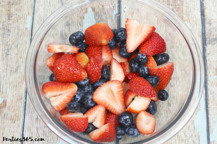 cut strawberries and blueberries in a glass bowl