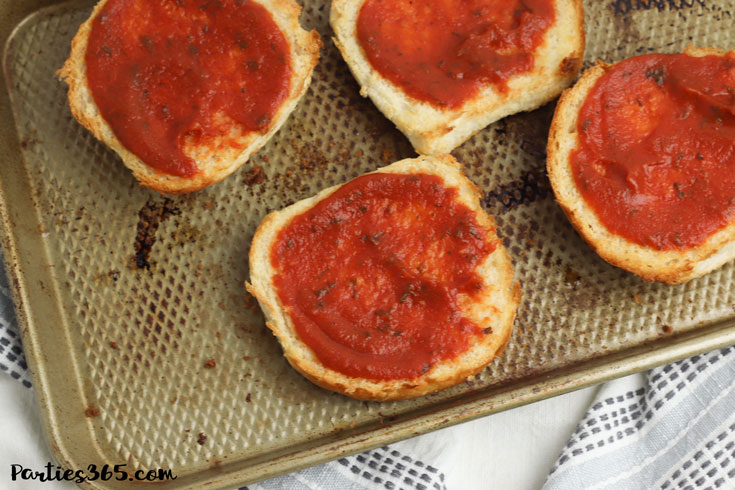 toasted buns topped with pizza sauce on a baking sheet