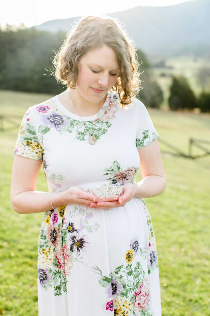 pregnant mom in floral dress in field holding a crown