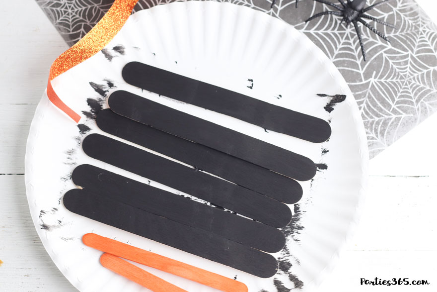 painted black and orange craft sticks on paper plate