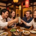 Four diverse friends raising glasses in a kanpai toast at a traditional Japanese izakaya