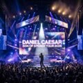 Daniel Caesar Son of Spergy Tour 2026 promotional concert artwork with arena stage lighting