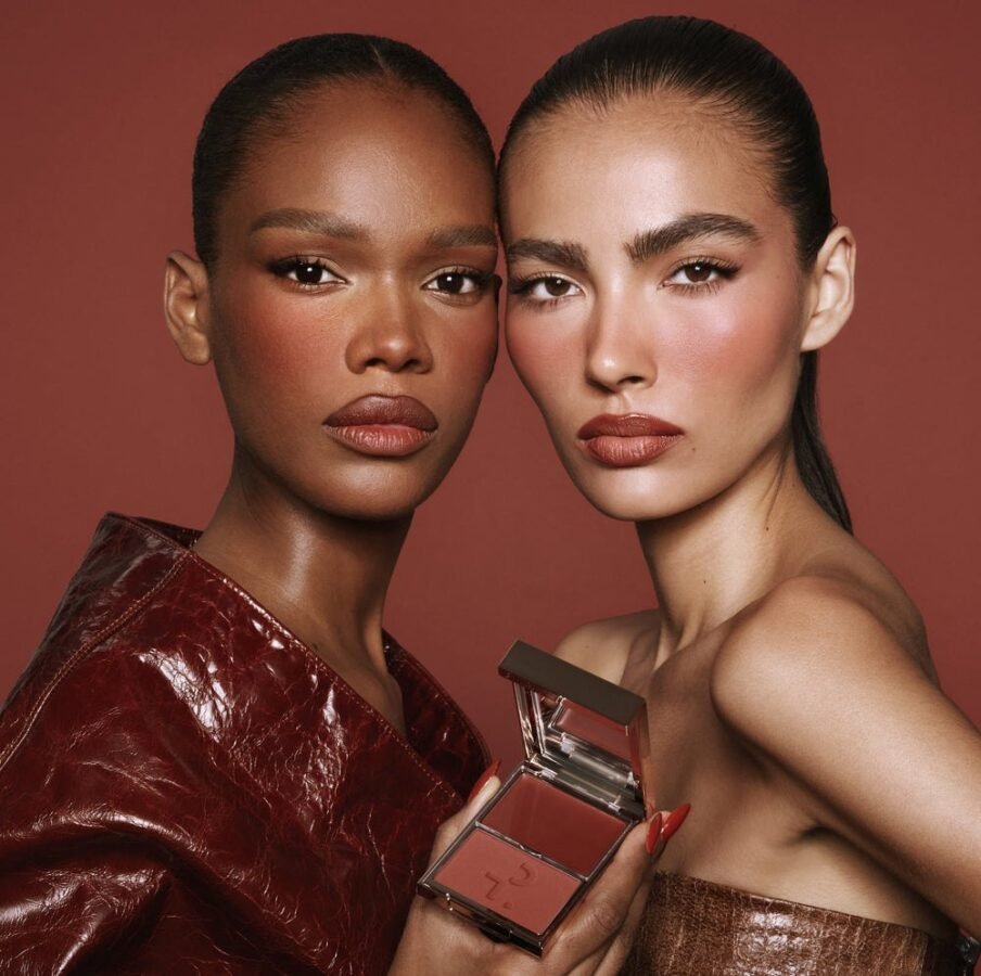 Two models wearing cream blush layered with powder, holding an open Patrick Ta Major Headlines compact