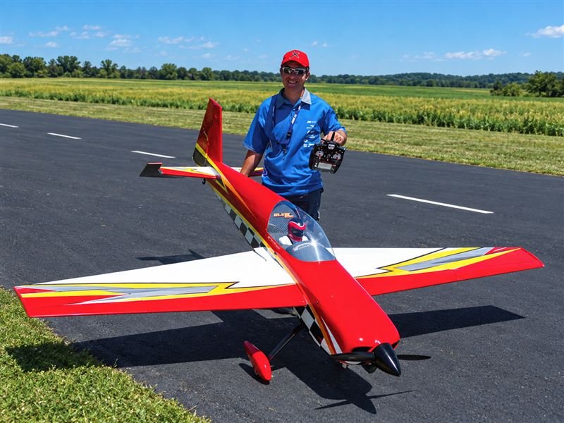RC hobbyist with a red remote-control airplane at an airfield